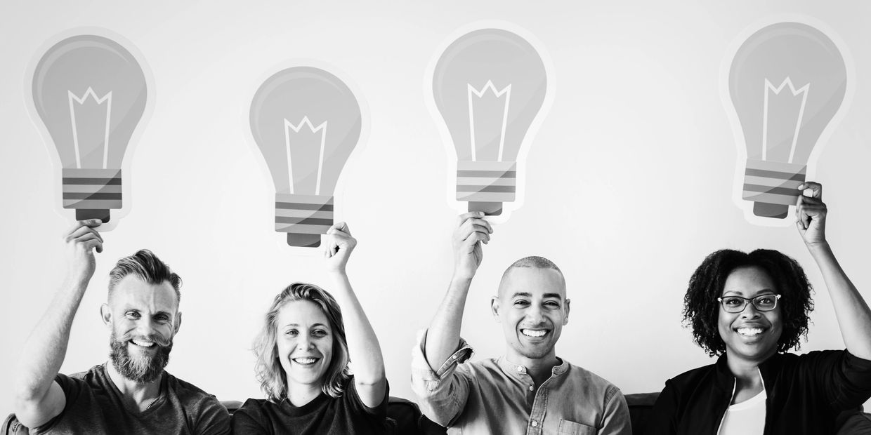 Four diverse people holding paper light bulbs representing ideas.