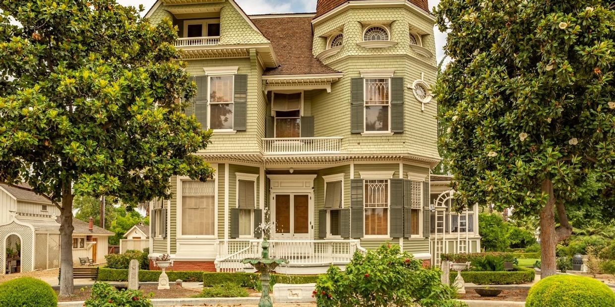 A large, elegant Victorian-style house surrounded by lush greenery and trees.