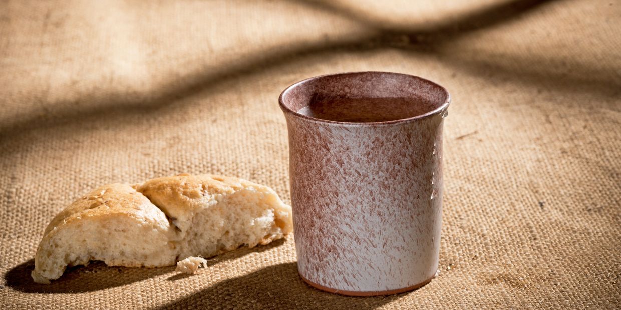 Rustic cup and bread slice on burlap under soft light.