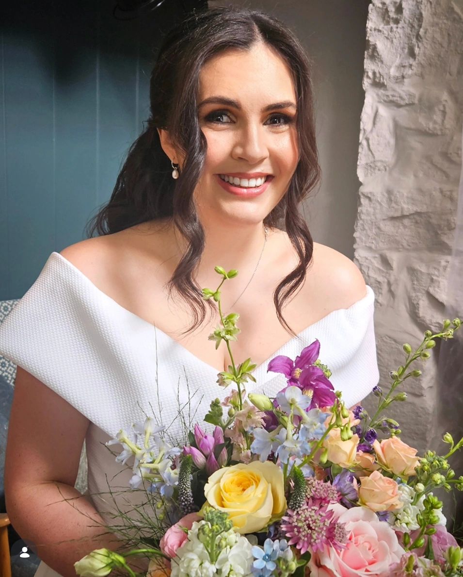 Smiling woman in white dress holding a bouquet of flowers.