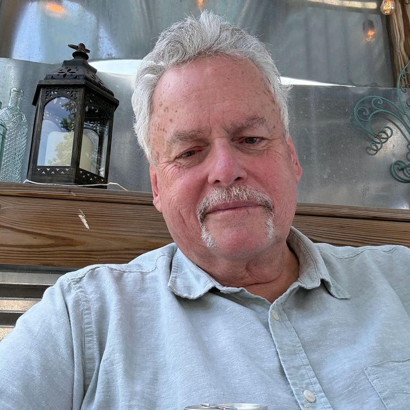 Older man with white hair and mustache, smiling indoors near a lantern.
