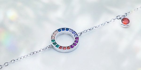 Silver bracelet with a colorful circular charm and a red gemstone accent.