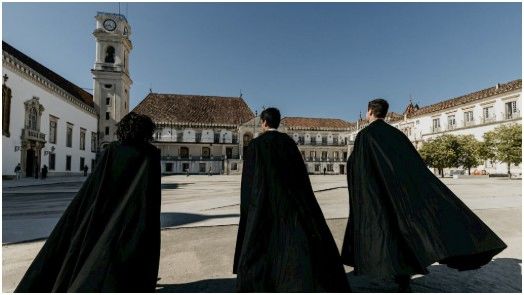 Three individuals in black cloaks in a historic square.