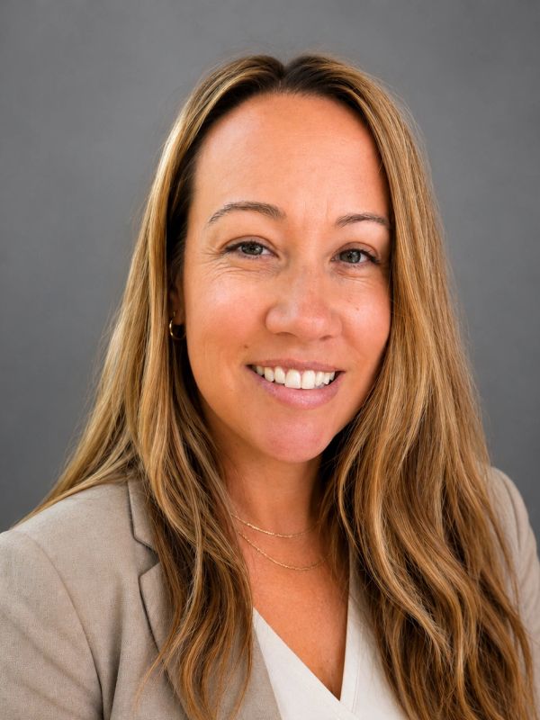 Smiling woman with long hair in a beige blazer against a gray background.