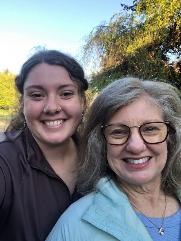 Two smiling women outdoors with greenery in the background.