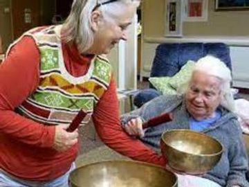 Woman healer helping elderly lady with pain using singing bowls
