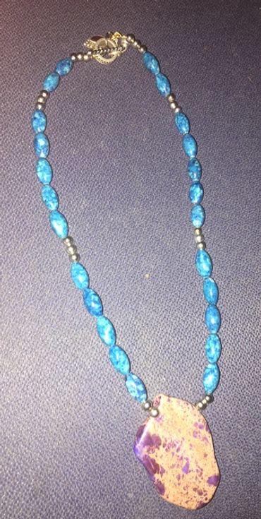 Blue beaded necklace with a large purple stone pendant.
