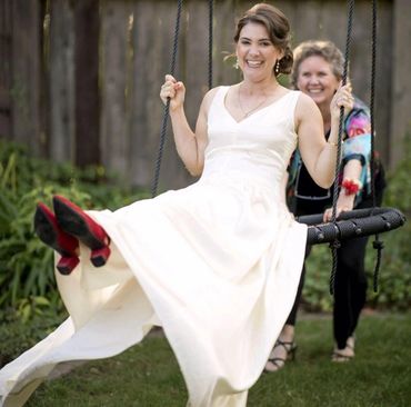 Bride joyfully swinging with a woman pushing her on a tire swing outdoors.