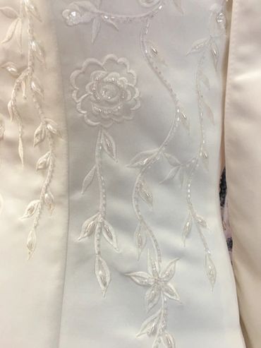 Close-up of white fabric with delicate floral embroidery and bead detailing.