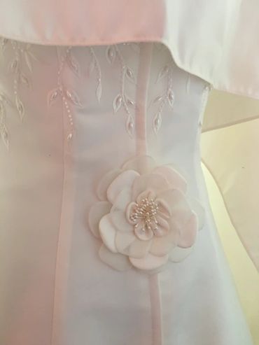 Close-up of a white dress with embroidered details and a fabric flower embellishment.