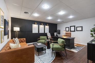 Modern office with a leather sofa, green chairs, and a sleek black desk.