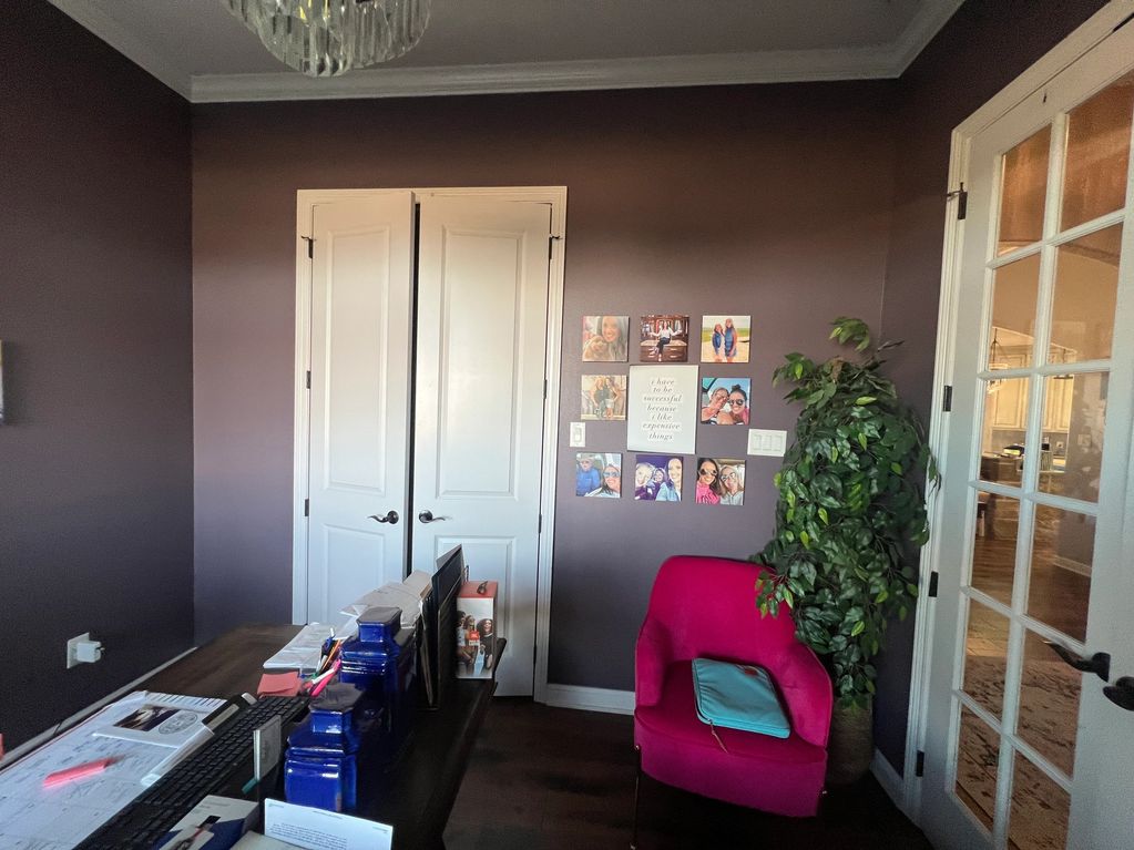 Cozy home office with purple walls, photo collage, red chair, and glass door.