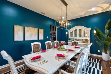 Elegant dining room with teal walls, white table, and decorative lighting.