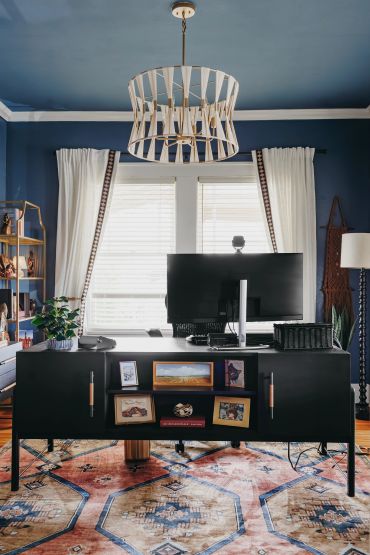 Modern home office with a black desk, dual monitors, and a stylish chandelier.
