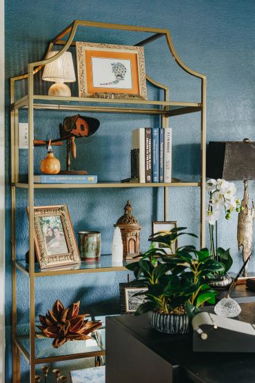 Elegant gold shelving unit with books, framed photos, and decorative items against a blue wall.