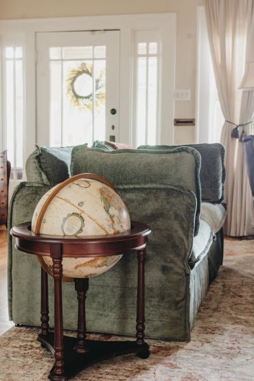 A vintage globe on a wooden stand beside a green couch in a cozy living room.