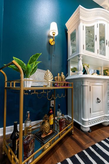 Elegant home bar setup with a gold cart, decorative items, and a white cabinet.