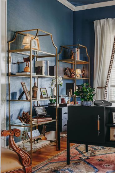 Elegant living room corner with gold metal shelves, decorative items, and a black cabinet.