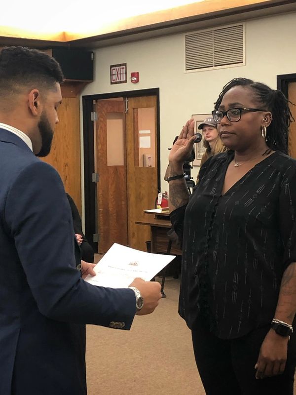 A woman is sworn in during a formal ceremony while a man reads from a document.