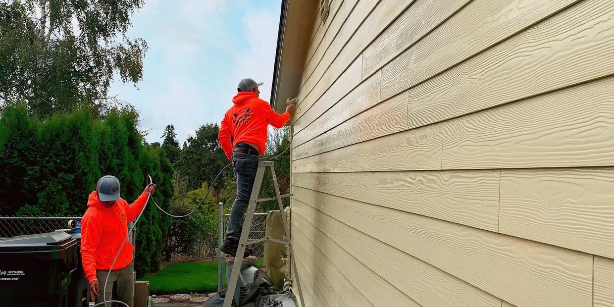 Image of two workers spray painting the side of a house. 