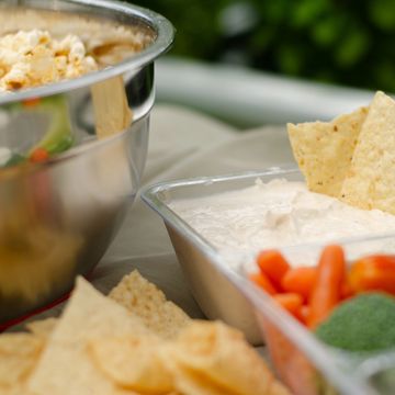 A tray of creamy dip with chips and fresh veggies on a table.