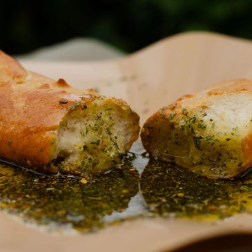 Garlic bread dipped in herb-infused olive oil on parchment paper.