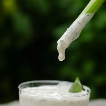 Close-up of creamy sauce dripping from a spoon into a glass with a green leaf.