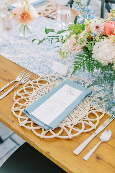 table setting with rattan charger, blue napkin, toile, and spring flowers