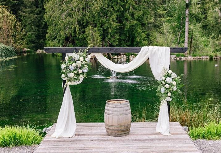 Wedding ceremony arbor at pond with white arbor drape and wine barrel