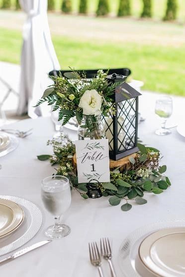 Wedding tablescape with wood slice, black lantern, table number and flowers.