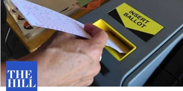 Close up of a hand feeding a ballot into a ballot machine.