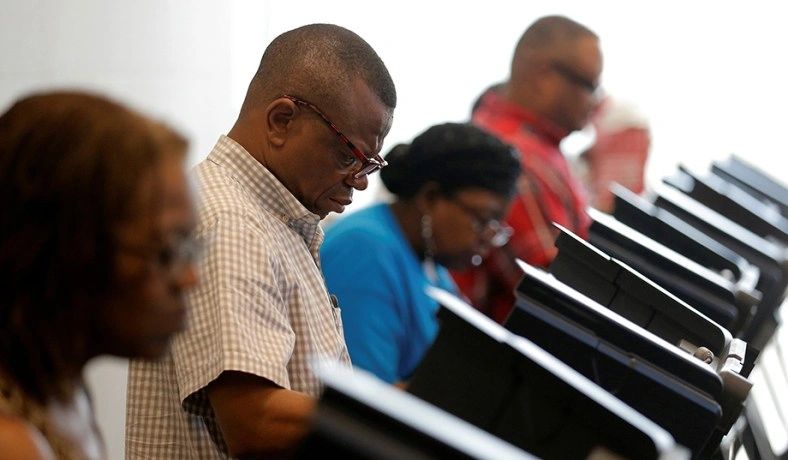 Closeup of four voters standing at voting booths.