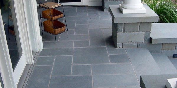 A modern porch with slate tile flooring and a small basket stand.
