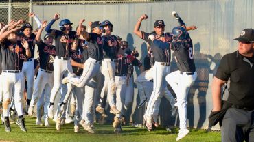 Baseball team in navy and white uniforms celebrating a victory together on the field.