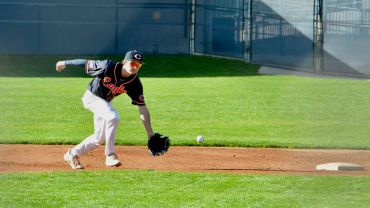 Baseball player in black jersey fields a ground ball near second base.