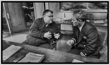 Two men engaged in an intense discussion at a wooden desk.