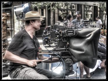 Cameraman operating a professional film camera outdoors with a focused expression.