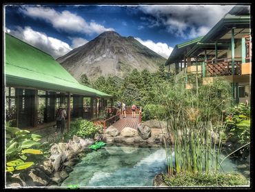 Mountain lodge with green roofs and pond in front, people enjoying nature.