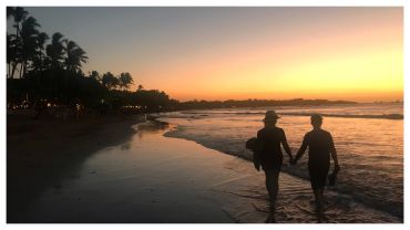 Couple holding hands walking along a beach at sunset.