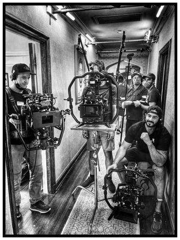 Film crew setting up cameras in a narrow hallway, captured in black and white.