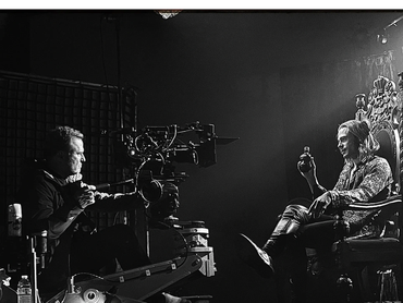 Black-and-white film set with a camera operator filming a man on an ornate throne.
