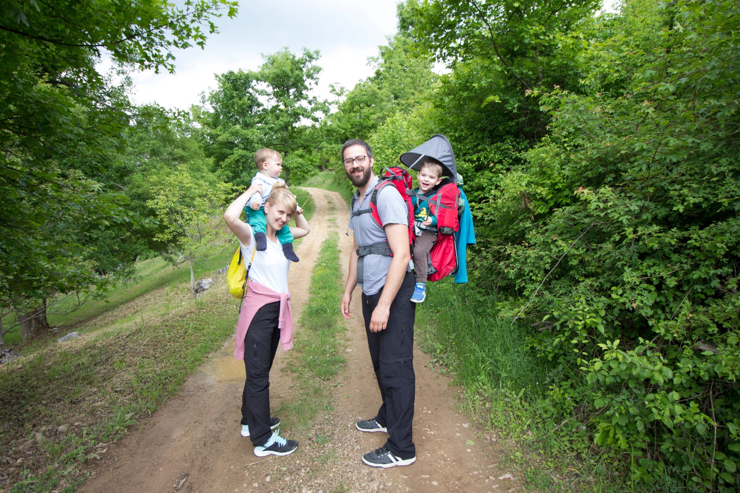 A family with two young children on a dirt path surrounded by trees.