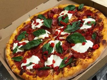 Fresh pizza with basil, mozzarella, and red pepper atop a golden crust in a delivery box.