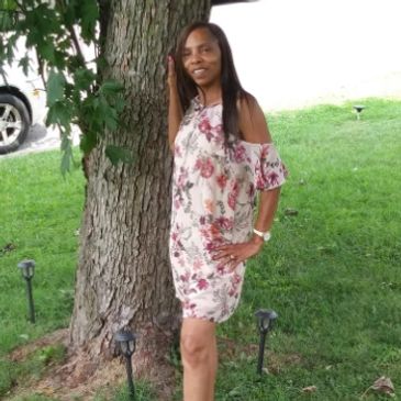 Woman in floral dress posing by a tree.