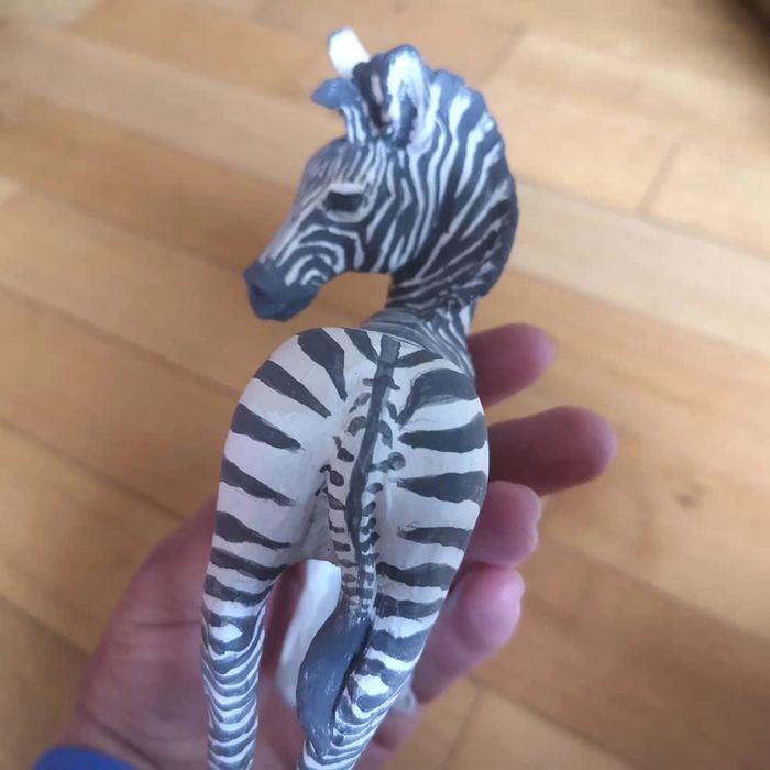 Close up of  the rear of a young zebra  ceramic sculpture being held in the potter's hand. 