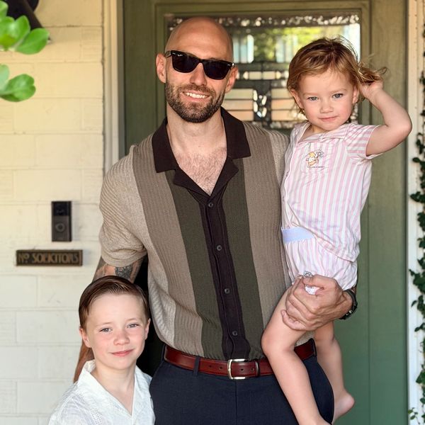 Man with sunglasses holding a child and standing next to another child, smiling.