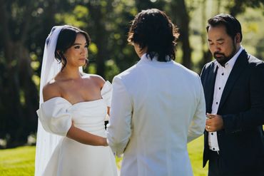 Bride and groom exchanging vows outdoors with officiant during wedding ceremony.