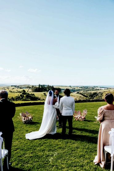 Outdoor wedding ceremony with bride, groom, and guests on a sunny day.