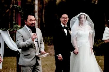 Couple holding hands during outdoor wedding ceremony with officiant speaking.