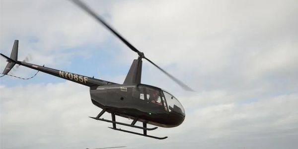 A black helicopter flying against a cloudy sky.